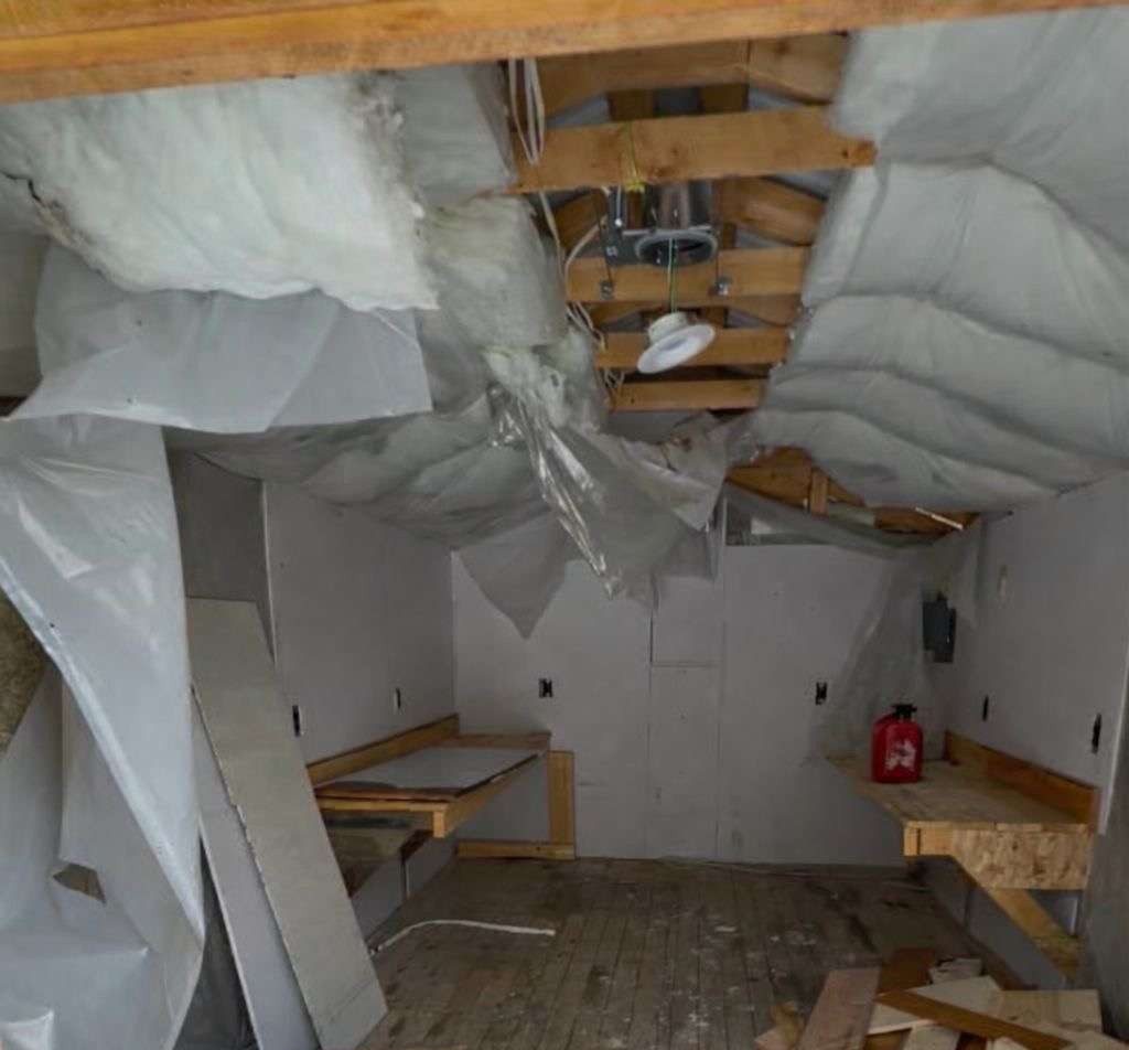 The outbuilding before the build, with exposed rafters, hanging insulation and plastic sheeting.