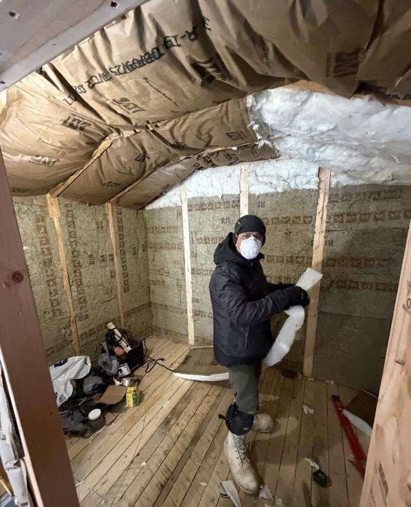 A builder in a mask insulating the walls and ceiling of the outbuilding.