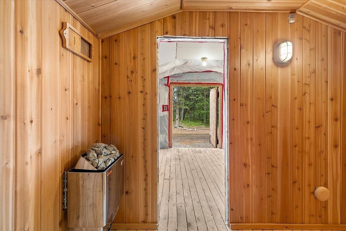 Sauna heater with stones against cedar walls, door open to the woods outside.