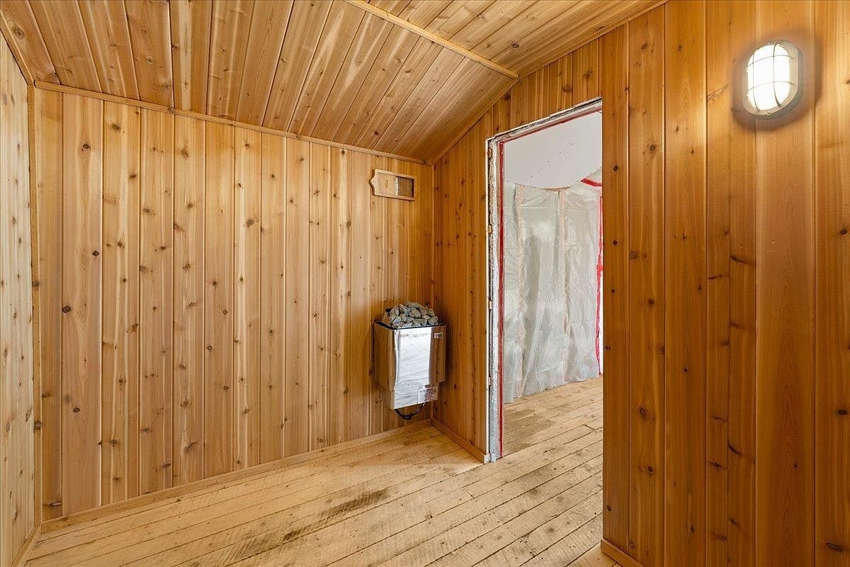Finished cedar-paneled sauna room with a wall-mounted heater and a wood floor.